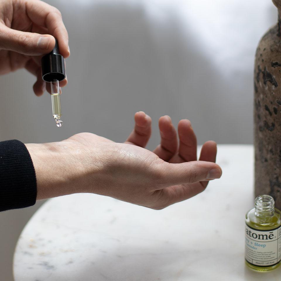 A woman applying some may chang essential oil to her wrist with a bottle on a table