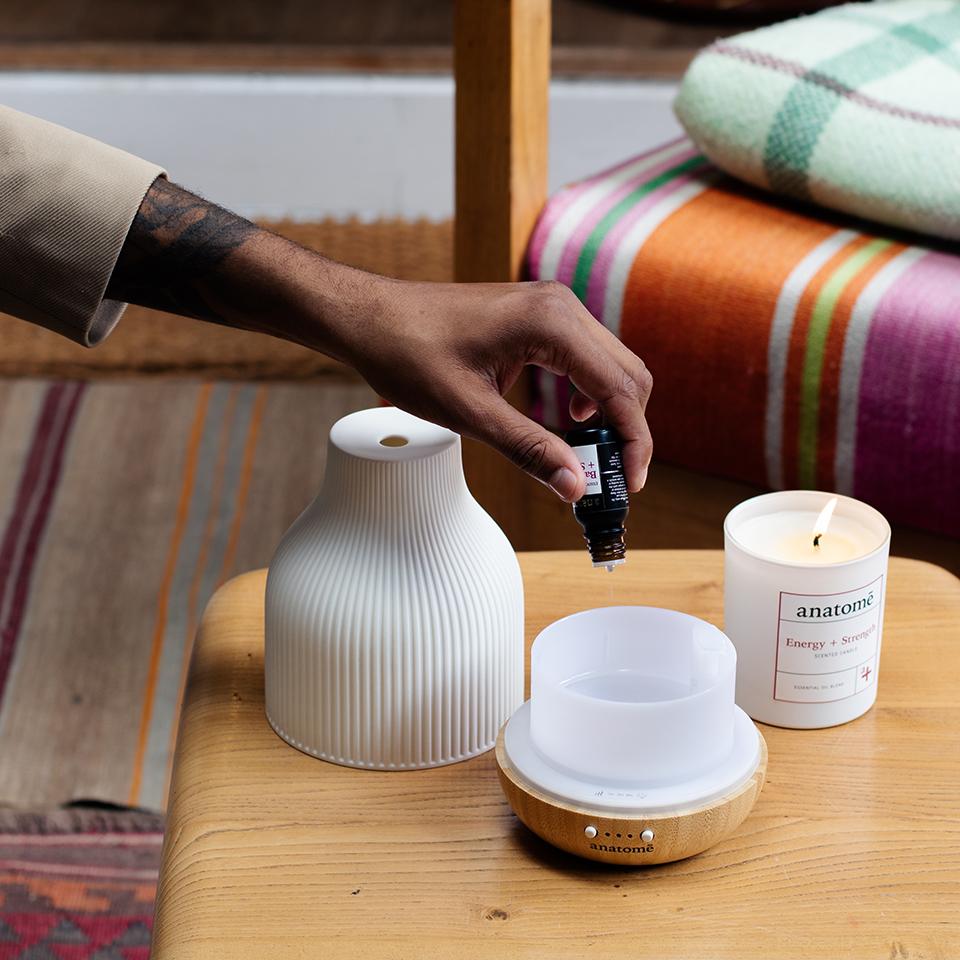 neroli essential oil being put into a ceramic oil diffuser on a wooden table