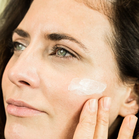 A woman rubbing a bottle of Organic Ultra Hydrating Face Moisturiser onto her cheek